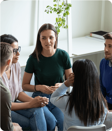 Five people sit in a circle indoors, engaged in conversation. One woman in a green shirt appears to be speaking about Suboxone Addiction Treatment while others listen attentively.