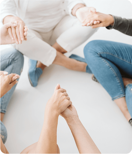 A group of people sits in a circle on the floor, holding hands, offering each other support during Medically Assisted Treatment sessions.