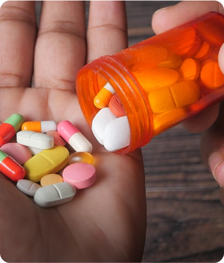 A hand holds assorted colorful pills as more spill from an orange prescription bottle, representing medically assisted treatment for opioid addiction.