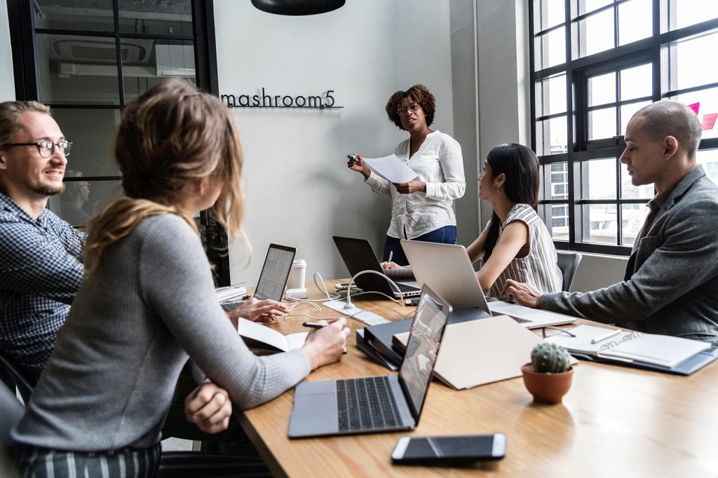 Five people in a modern office conference room, with one person standing and presenting to four seated colleagues around a table with laptops and papers, discussing advancements in opioid addiction treatment.